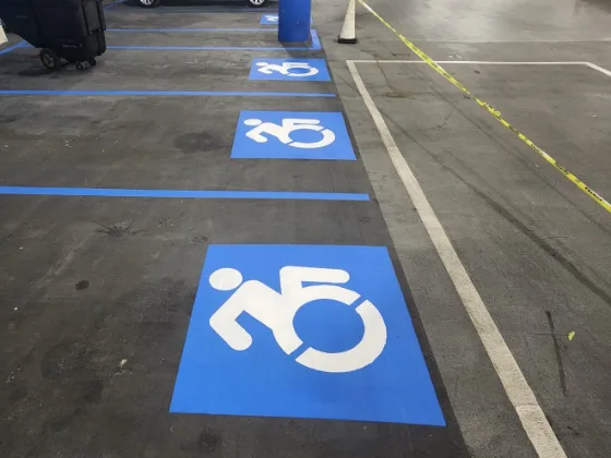 Three freshly re-marked blue accessible-stall stencils in a row down a parking garage deck, blue lines dividing the bays and a white drive-lane line running along the right