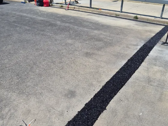 Fresh black asphalt repair strip filling a long joint through a weathered concrete parking deck