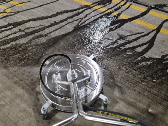 Rotary surface cleaner on a parking garage deck, dirty water streaming off the concrete it has just cleaned beside a yellow lane line