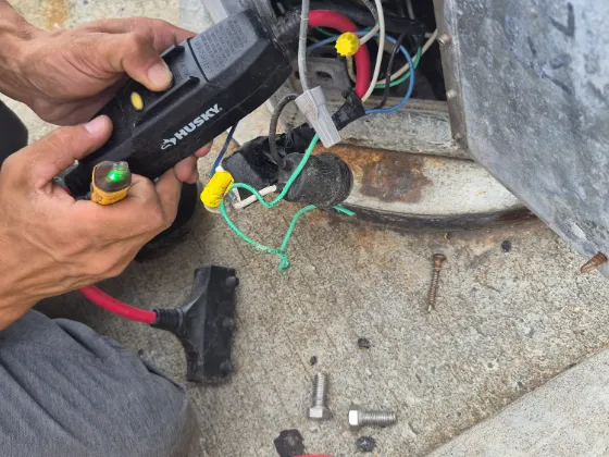 Hands holding a voltage tester against the wiring at the base of a commercial gate operator, loose bolts on the concrete alongside