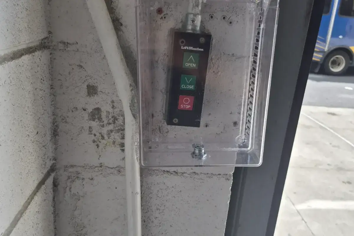 Open, close and stop gate control station behind a clear protective cover on a block wall beside a garage entrance