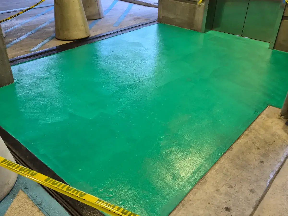 Freshly applied green traffic-deck coating across a parking garage bay, still wet and taped off with caution tape