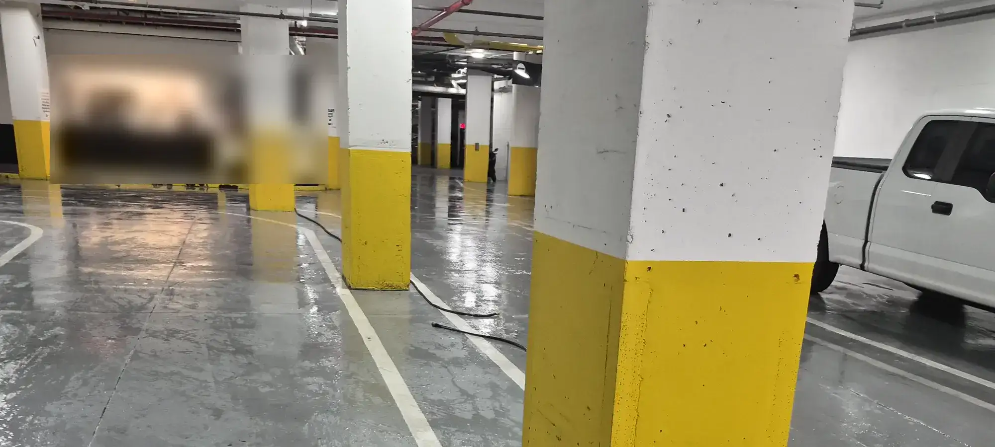 Freshly washed parking garage deck, wet grey concrete and white lane lines running between yellow-banded support columns