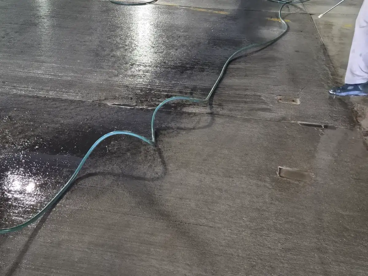 Water hose running across a concrete parking deck mid-wash, the washed section dark and wet