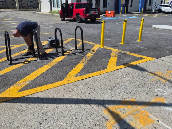 Crew member bolting down a bike rack on a commercial lot marked with fresh yellow hatching, safety bollards and accessible bays behind