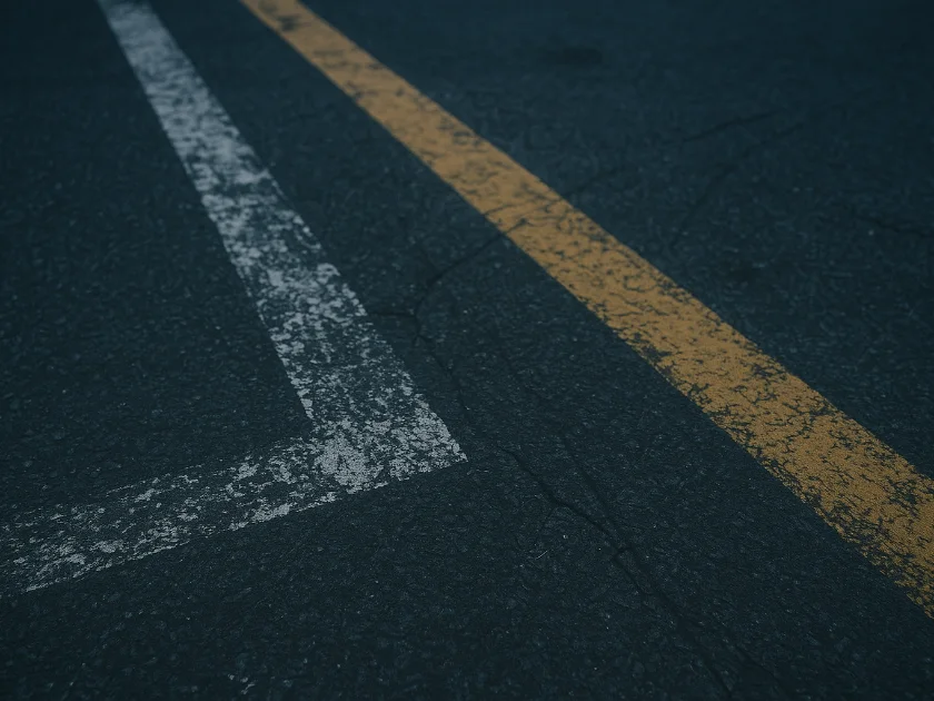 White stall line broken into patchy fragments beside a chipped yellow lane line on dark asphalt