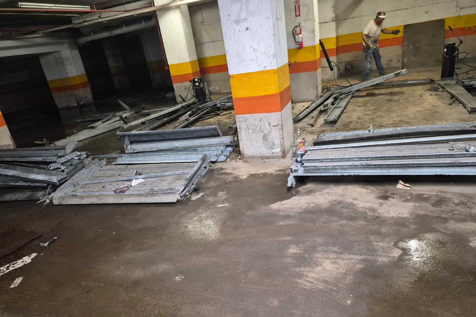 Parking stacker sections laid out flat across a garage deck beside the stripped bays they came out of, a crew member working at the far wall