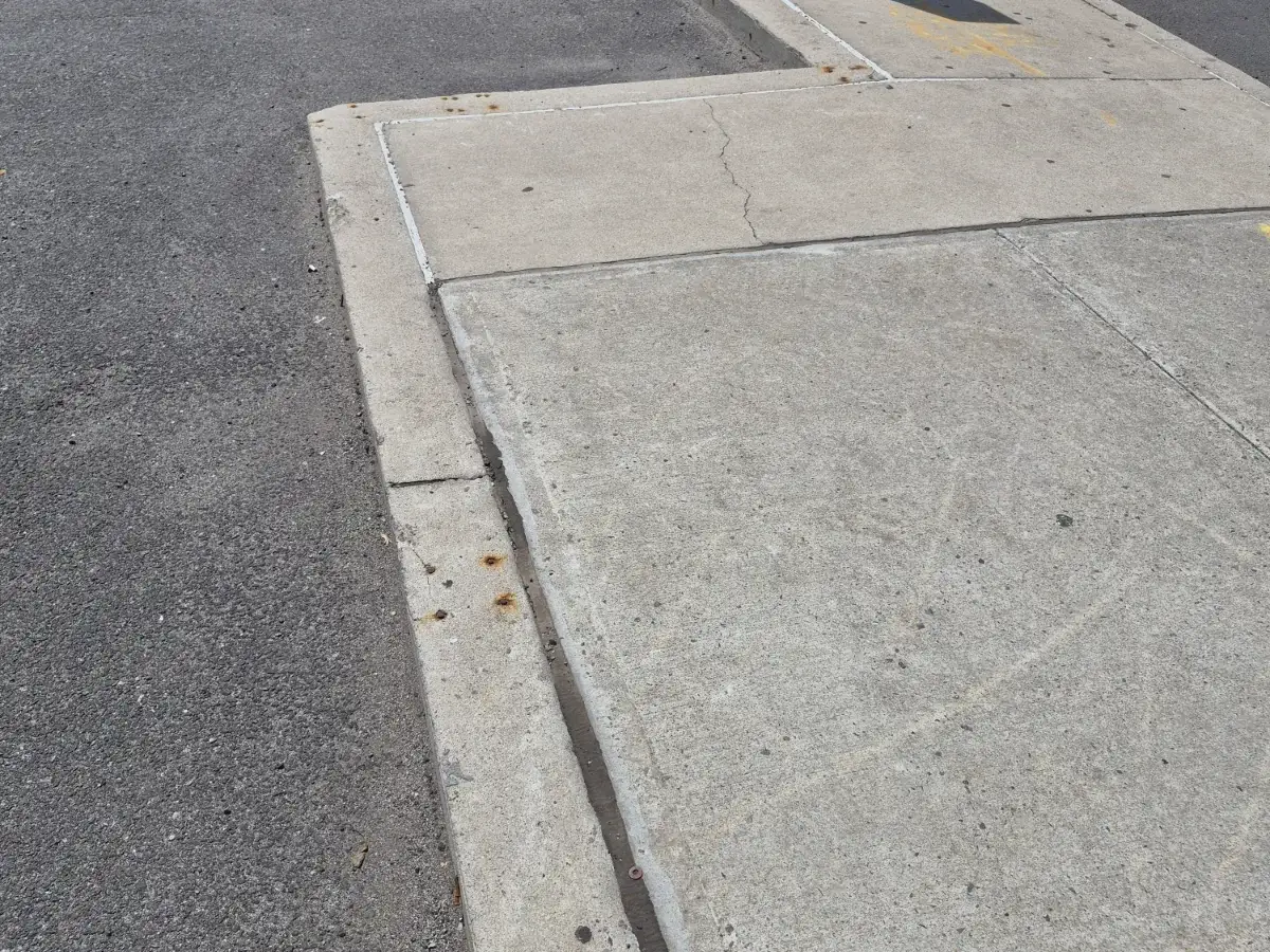 Open joint where dark asphalt meets a concrete pad at the edge of a parking area