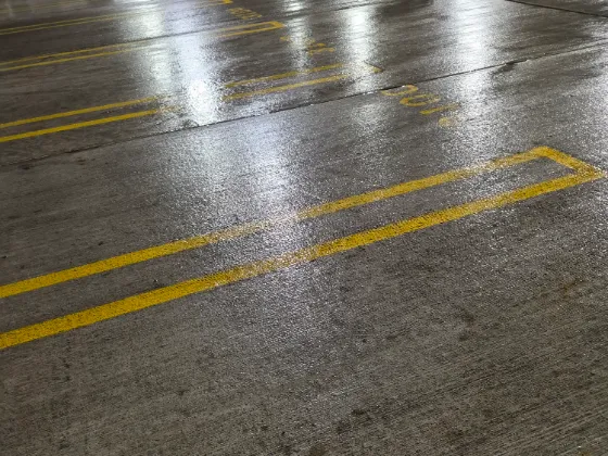 Parking garage deck after pressure washing, wet clean concrete with bright yellow lane markings and floor stencils
