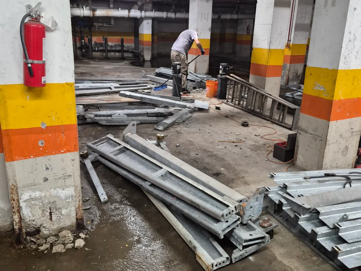 Crew member breaking down galvanised parking stacker frames stacked across a commercial garage deck between banded concrete columns