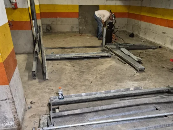 Crew member breaking down the last lifting post of a parking stacker in a stripped garage bay, base rails and cross members already unbolted and lying on the deck
