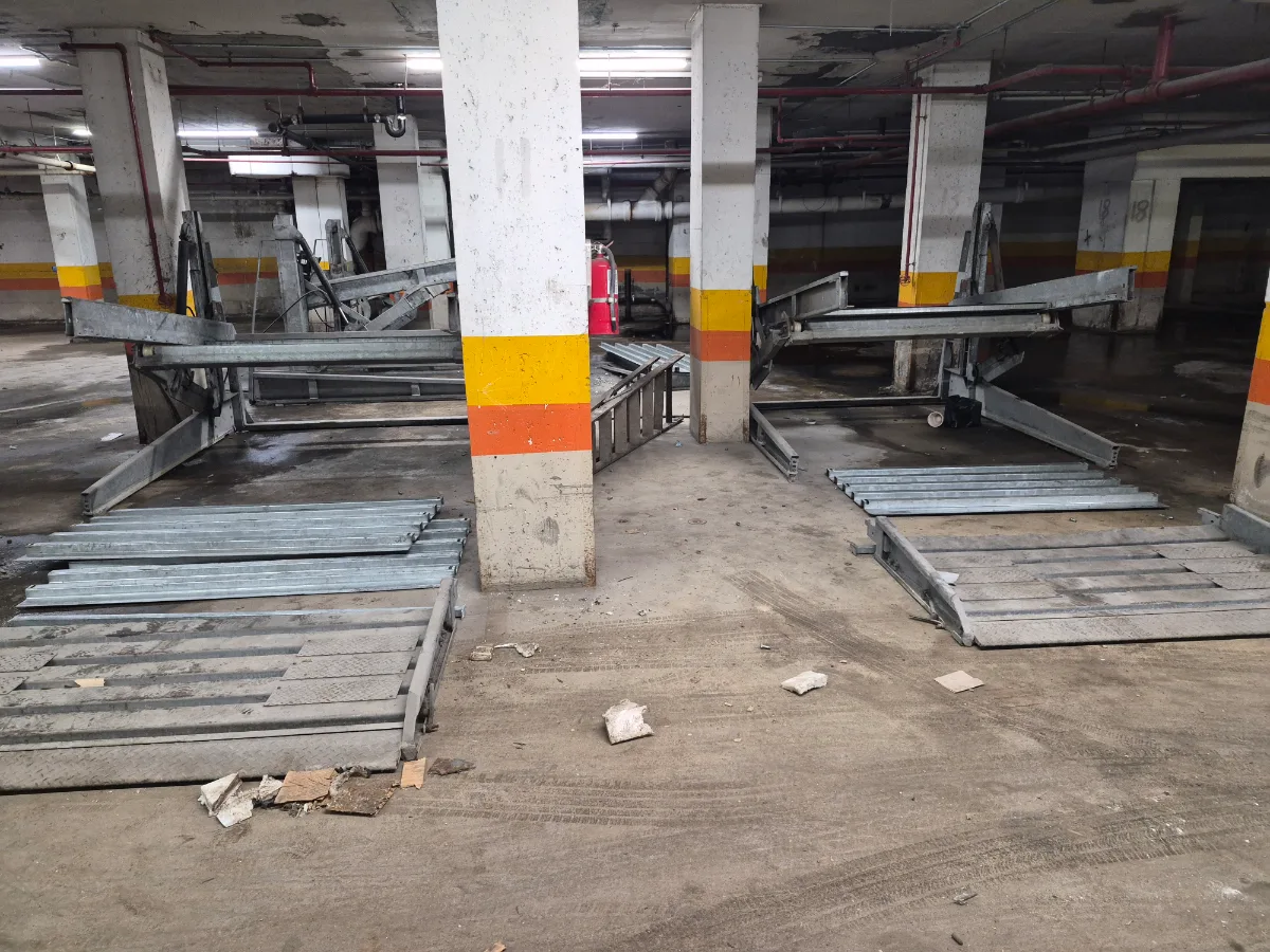 Two parking stacker systems part way through removal, platforms and cross members laid out flat across the bays under the banded columns of a garage