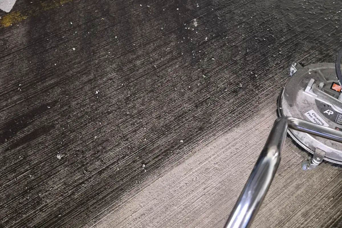 Rotary surface cleaner working across a streaked concrete parking deck