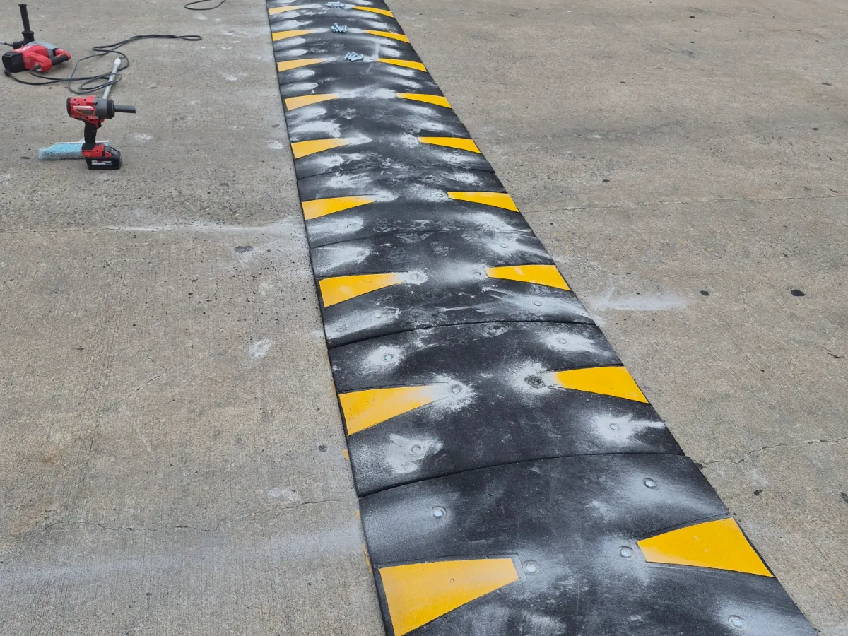 Newly bolted-down rubber speed bump with yellow chevrons on a concrete parking deck, impact driver and hammer drill beside it