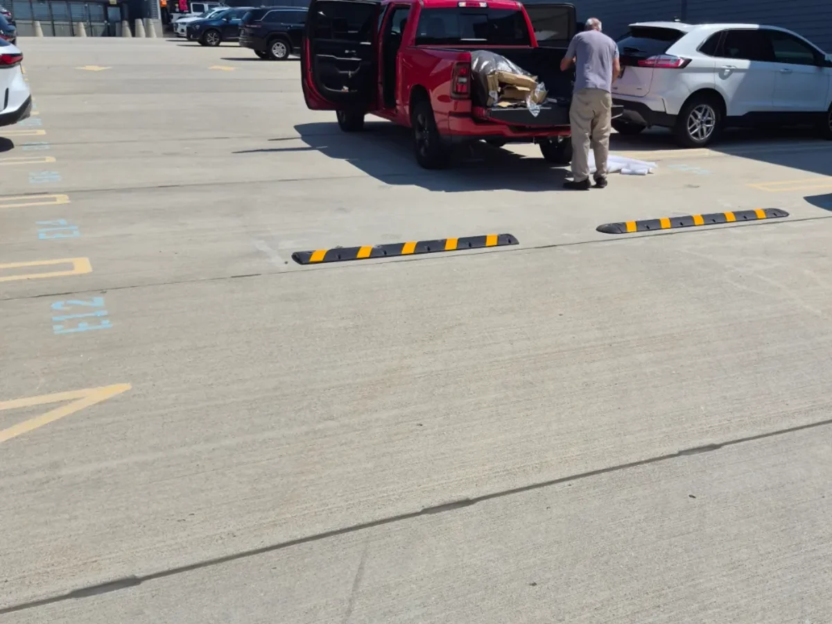 Crew member unloading rubber speed bumps from a pickup bed, two of them already laid out across a concrete parking lot