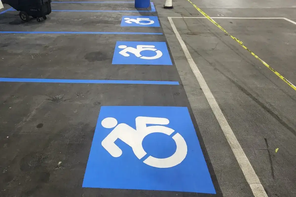 Three freshly re-marked blue accessible-stall stencils in a row down a parking garage deck, blue lines dividing the spaces