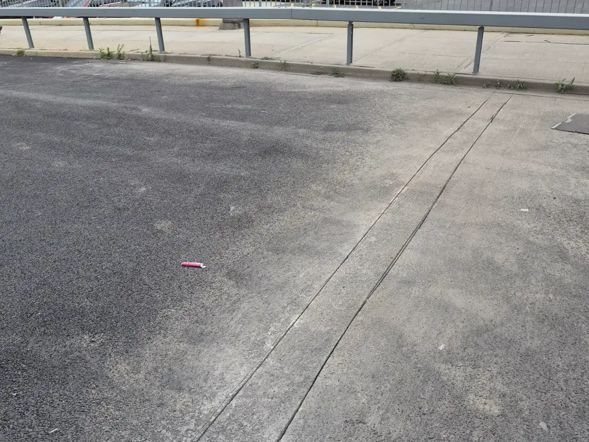 Weathered gray asphalt parking area with a long seam running across it below a steel guard rail