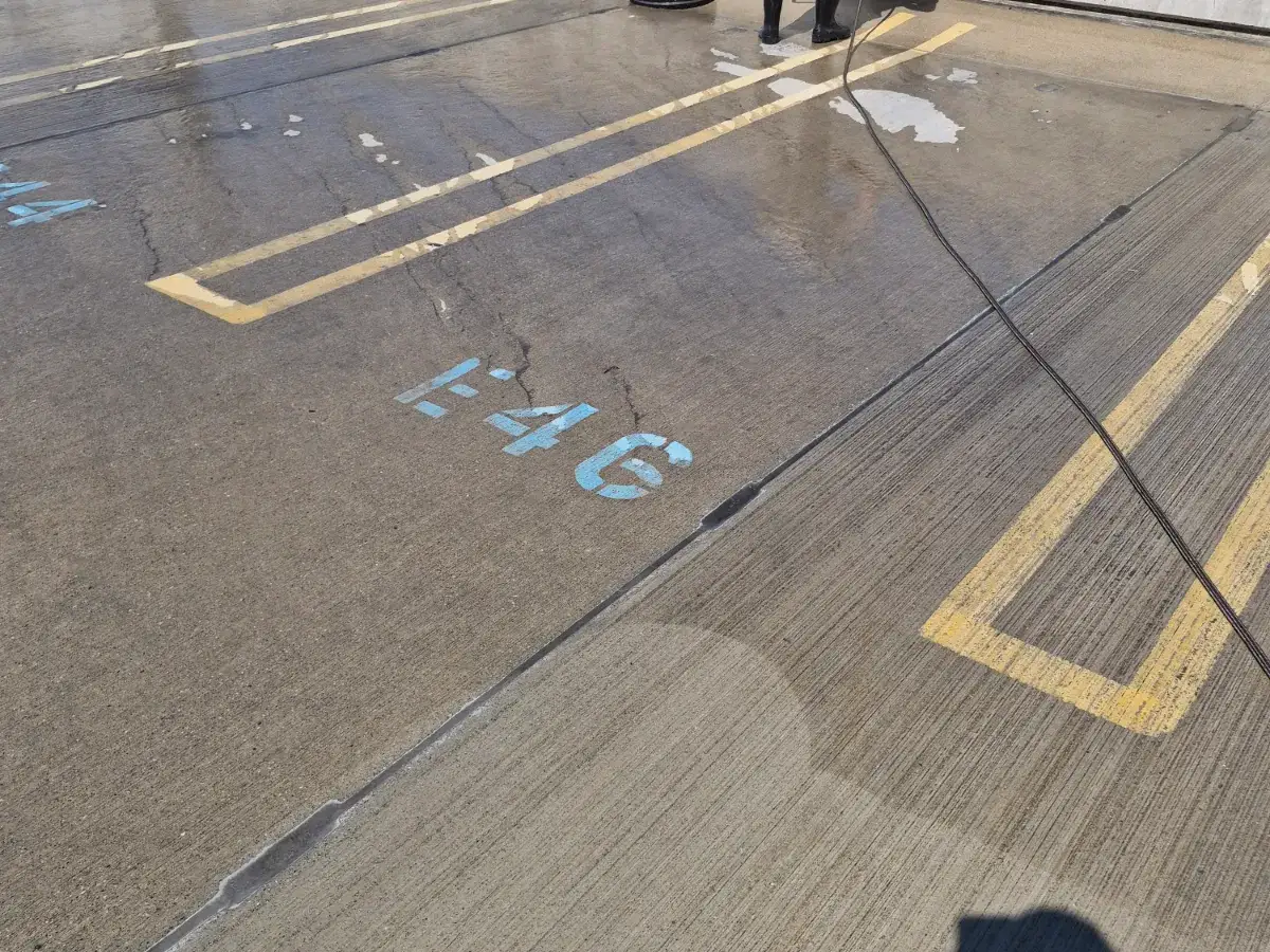 Worn yellow stall lines and a faded blue space number on a wet concrete parking deck