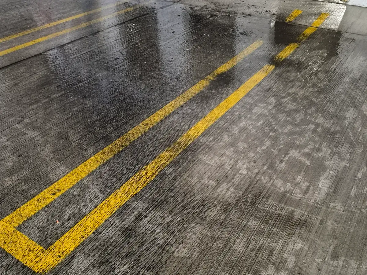Freshly painted yellow double stall lines on a wet, broom-finished concrete parking deck