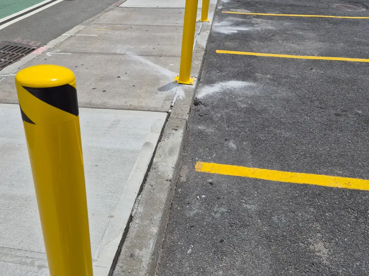 Yellow steel safety bollards with black reflective bands set along a sidewalk curb beside freshly striped yellow parking stalls